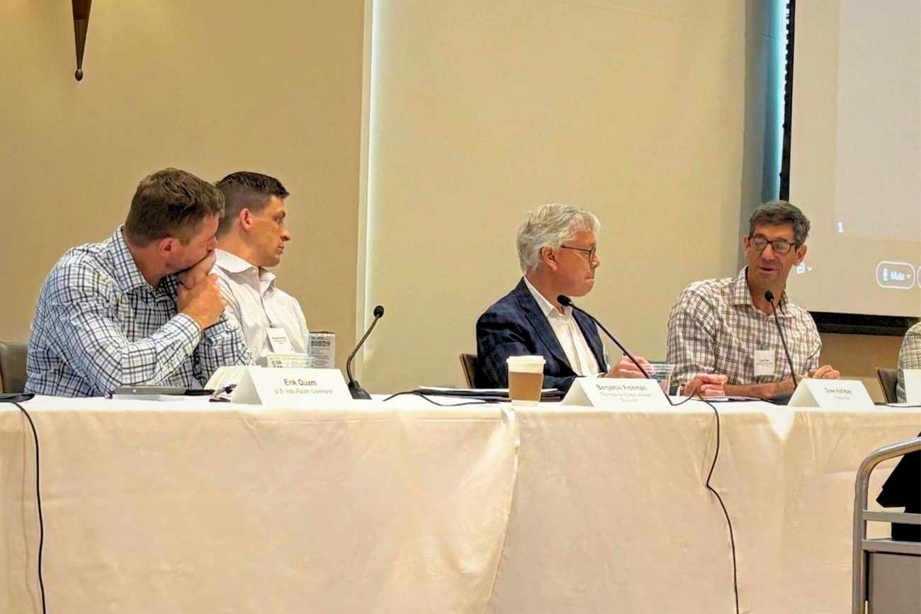 men speaking on a panel at a conference